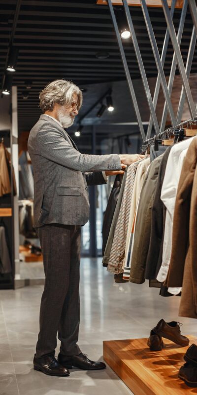 A man browsing clothes in a modern boutique store with a variety of suits on display.