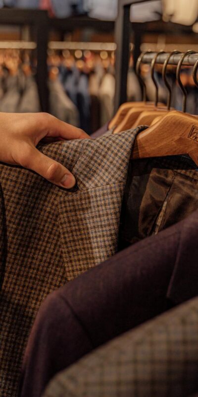 Close-up of a hand selecting men's blazers in a fashion store, highlighting trendy styles.